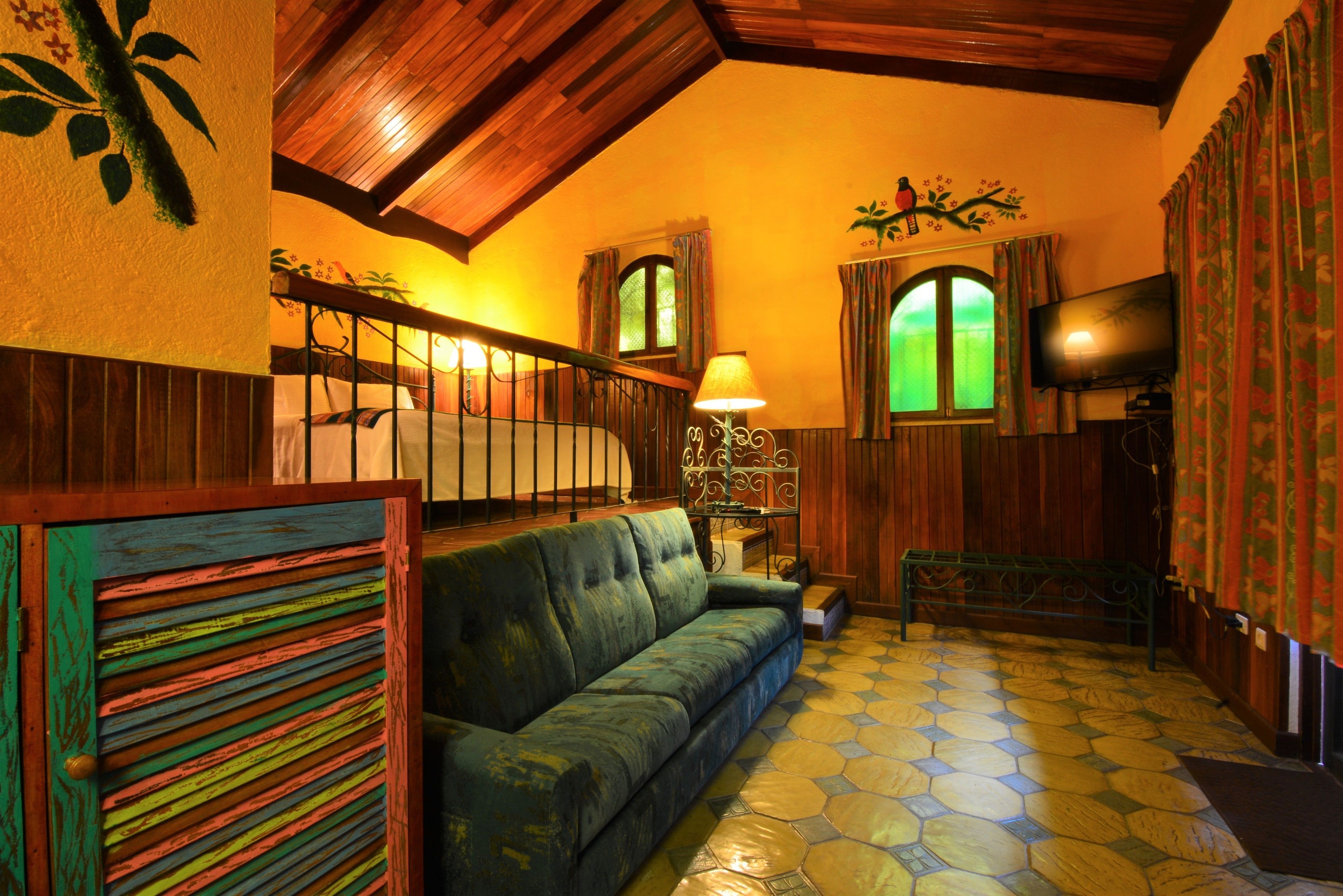 A cozy room with a green sofa, a wooden staircase, a television, and a patterned floor.