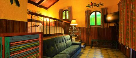 A cozy room with a green sofa, a wooden staircase, a television, and a patterned floor.