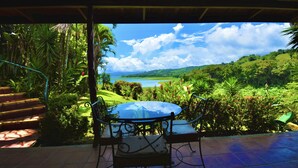 A covered patio with a glass table and chairs, overlooking a lush garden and a view of the sea. - La Mansion Inn Arenal (Arenal)