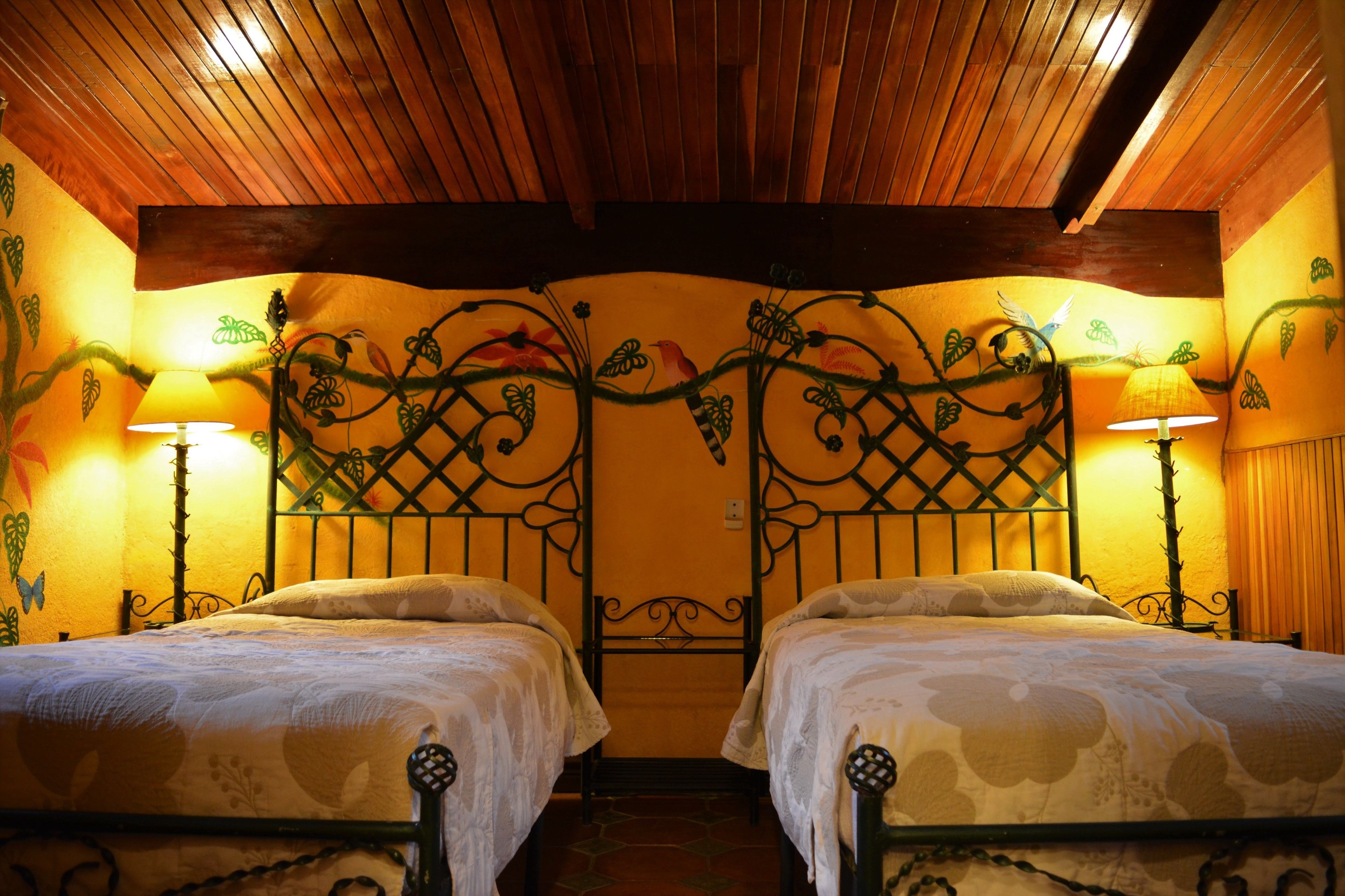 Una habitación con dos camas, techo de madera y murales en las paredes.