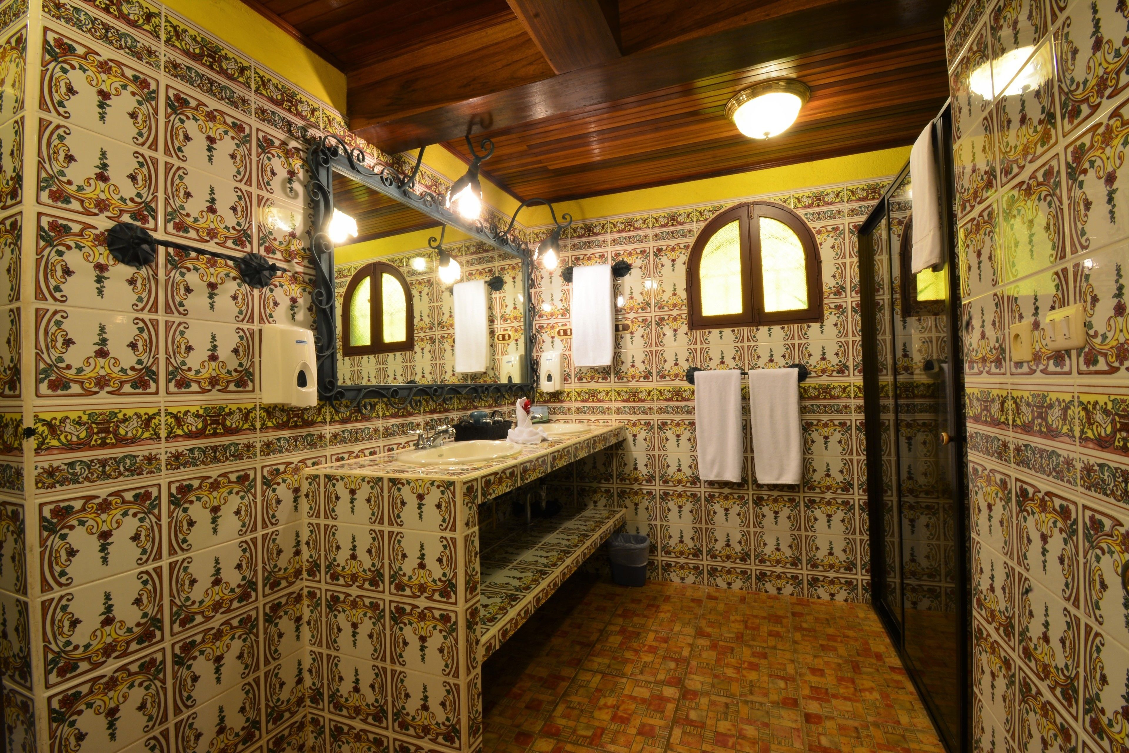 A bathroom with ornate tiled walls, a wooden ceiling, and a sink with a mirror above it.