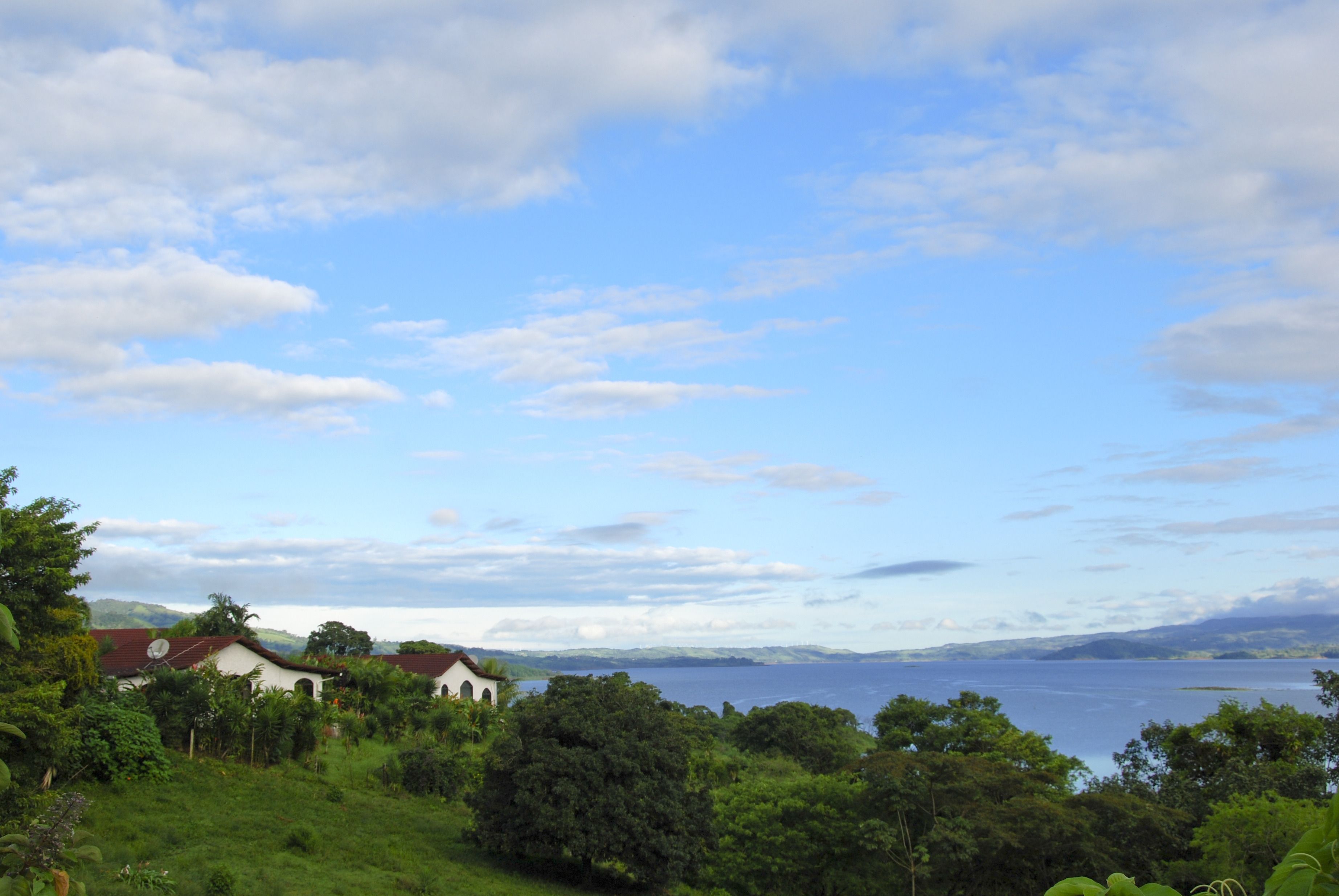 A coastal landscape with a white building with a red roof, surrounded by lush greenery and overlooking a body of water.