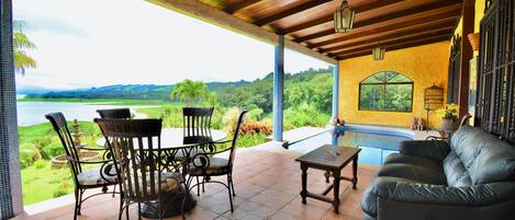 A covered patio with a dining set, a sofa, and a view of a lake and hills.