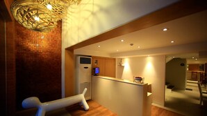 A reception area with a modern design, including a reception desk, a unique white bench, and a decorative ceiling light fixture. - Silom One (Bangkok)