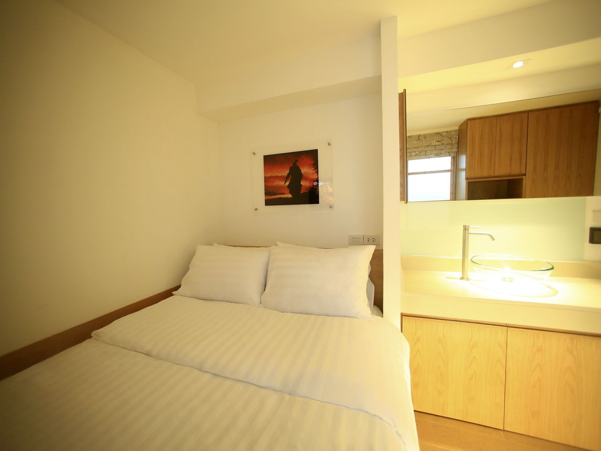 Ein Hotelzimmer mit Bett, einem Bild an der Wand und einem Badezimmer mit Waschbecken und Spiegel.