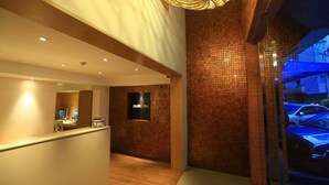 A modern reception area with a computer desk, a mounted TV, and a brick wall. - Silom One (Bangkok)