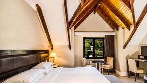 Habitación de hotel con una cama grande, un escritorio, una silla y una ventana con vistas a zonas verdes.