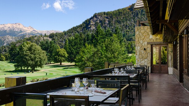Un espacio de comedor al aire libre con mesas y sillas, con vistas a un campo de golf y montañas.