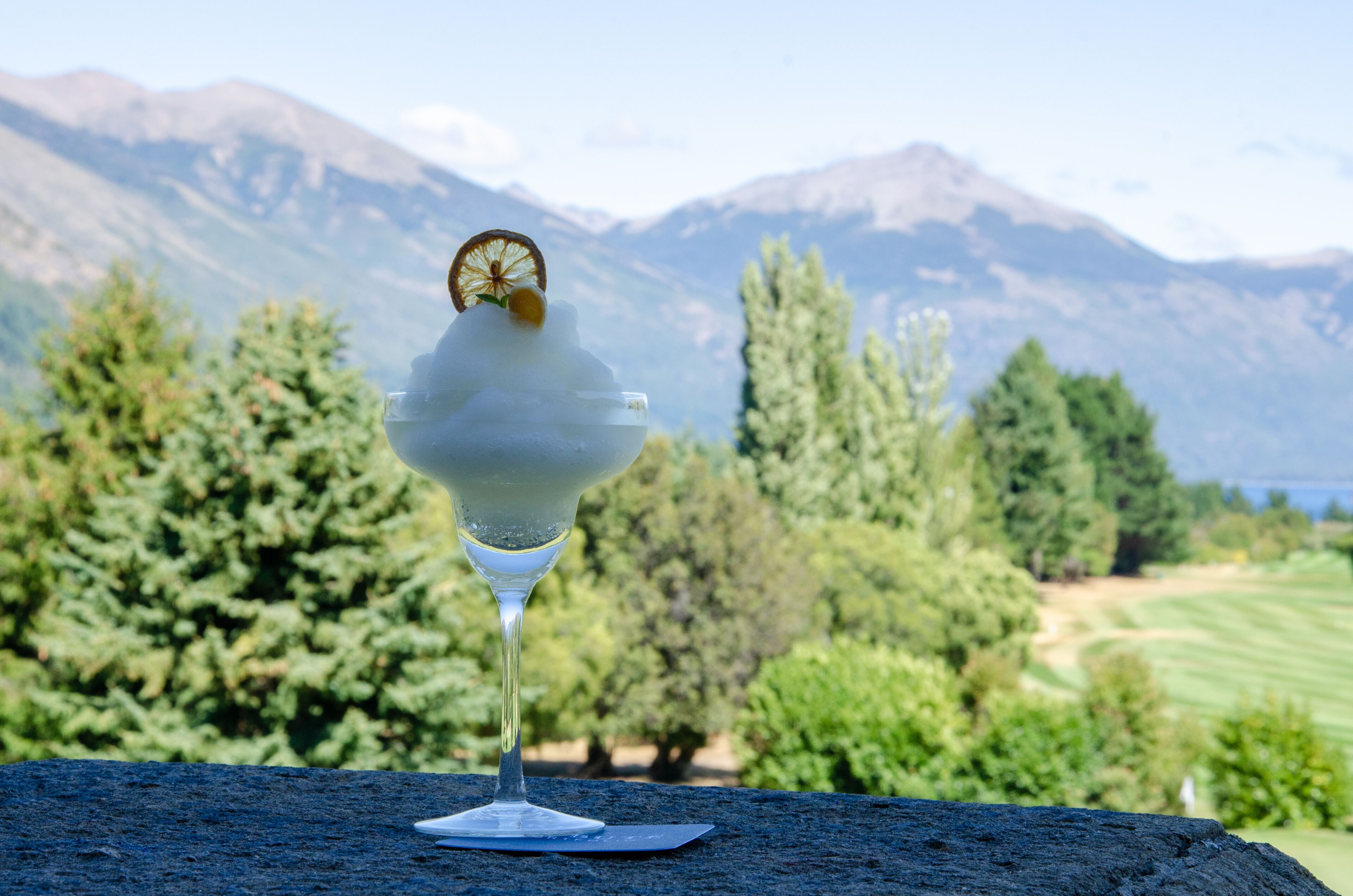 Ein Cocktailglas mit Zitronenzeste auf einem Tisch, im Hintergrund eine schöne Berglandschaft.