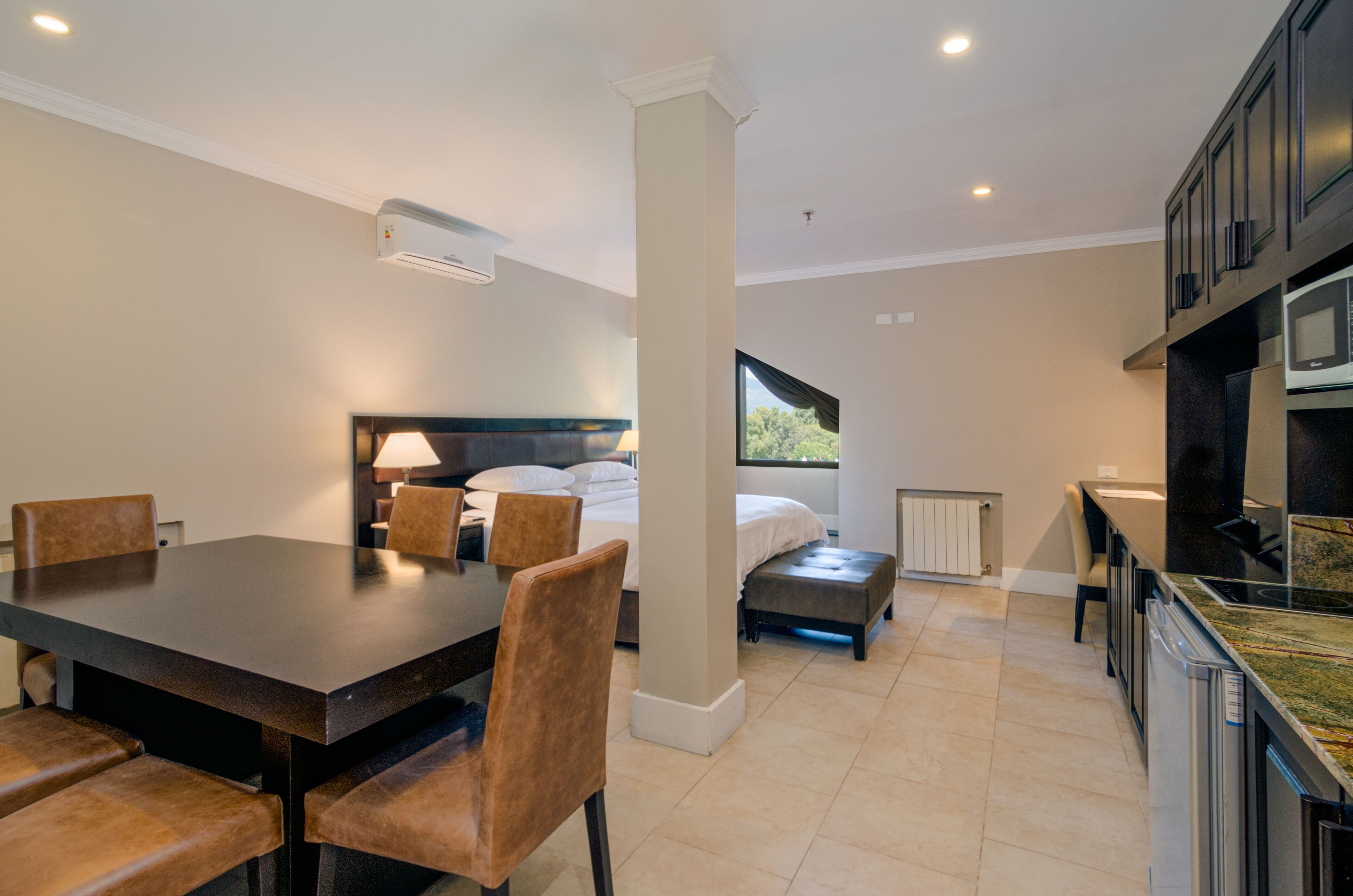 Een moderne hotelkamer met een zithoek, een bed met hoofdeinde, een raam met uitzicht en een kitchenette.