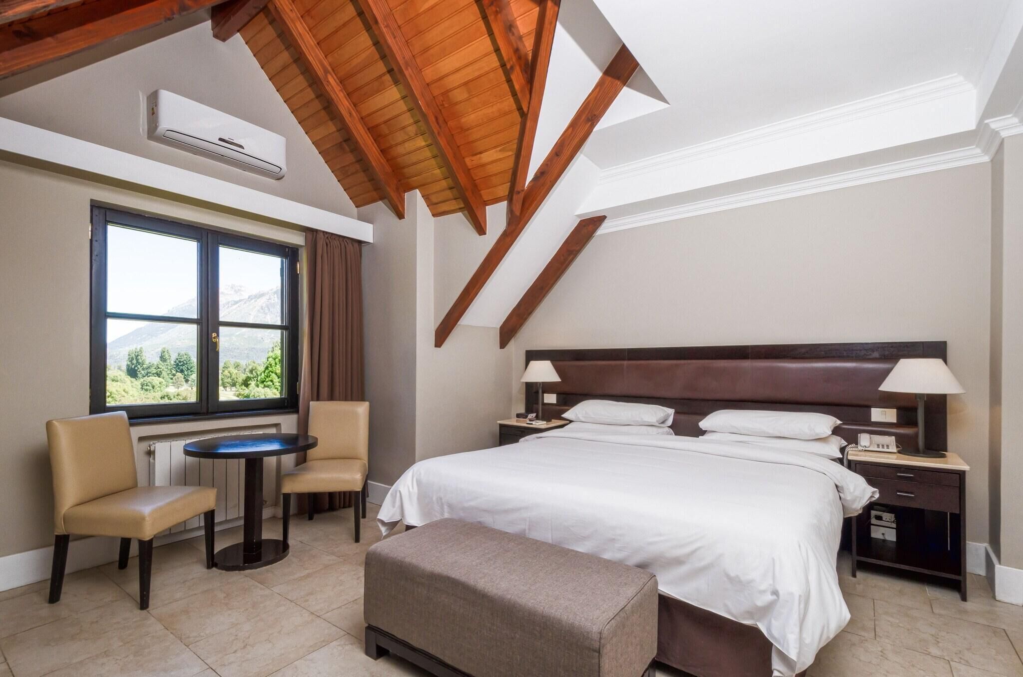 Habitación de hotel con una cama grande, un escritorio, una silla, una mesa redonda y vistas al exterior.