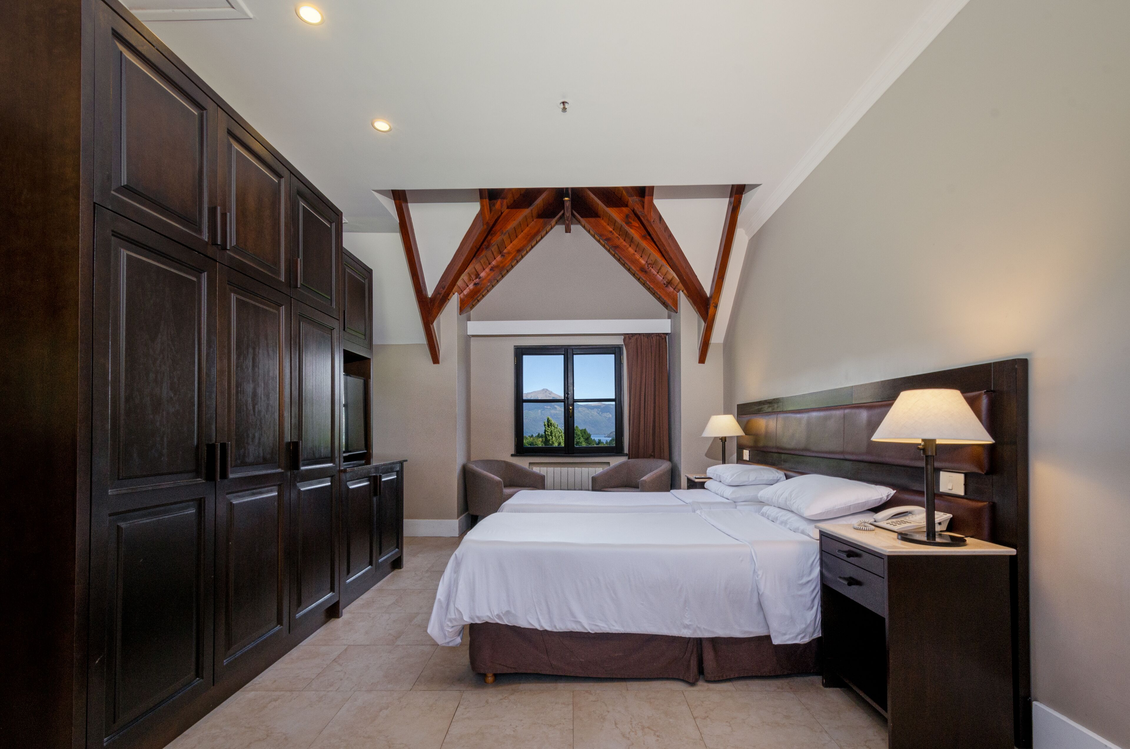 A bedroom with a large bed, two bedside tables, a nightstand, and a window with a view.
