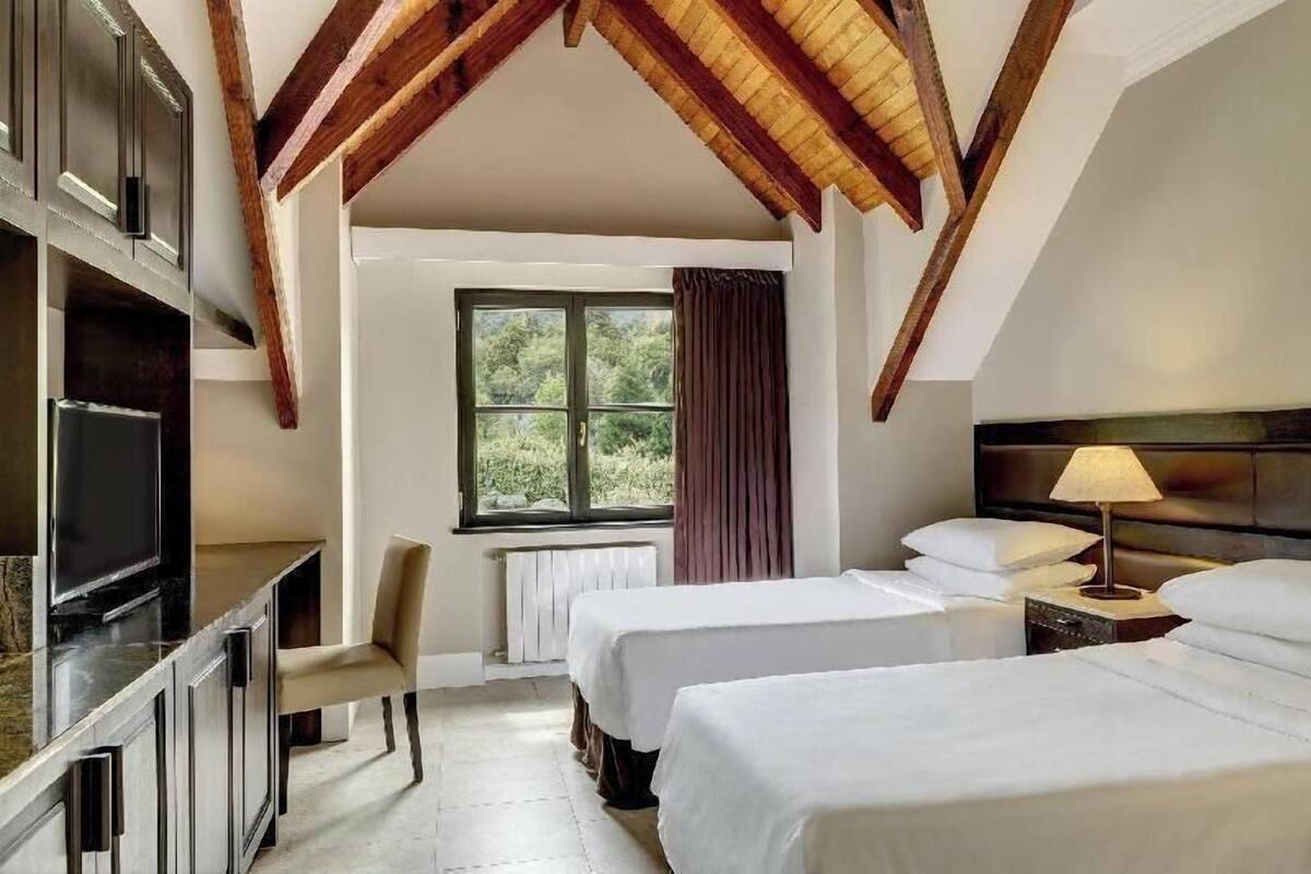 Habitación de hotel con dos camas, televisión, escritorio y ventana con cortinas.