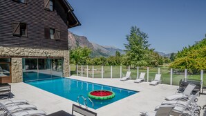 Una piscina con sillones de descanso, un muro de piedra y vistas a la montaña.