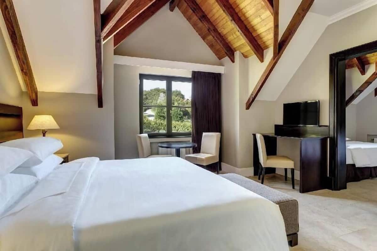 Habitación de hotel con una cama grande, un escritorio, una silla, un televisor y una ventana con vistas.