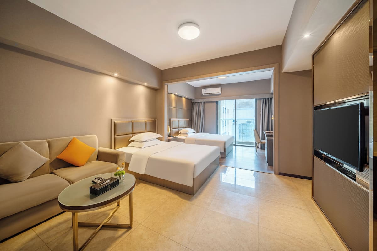 A hotel room with a sofa, two beds, a TV, and a coffee table.