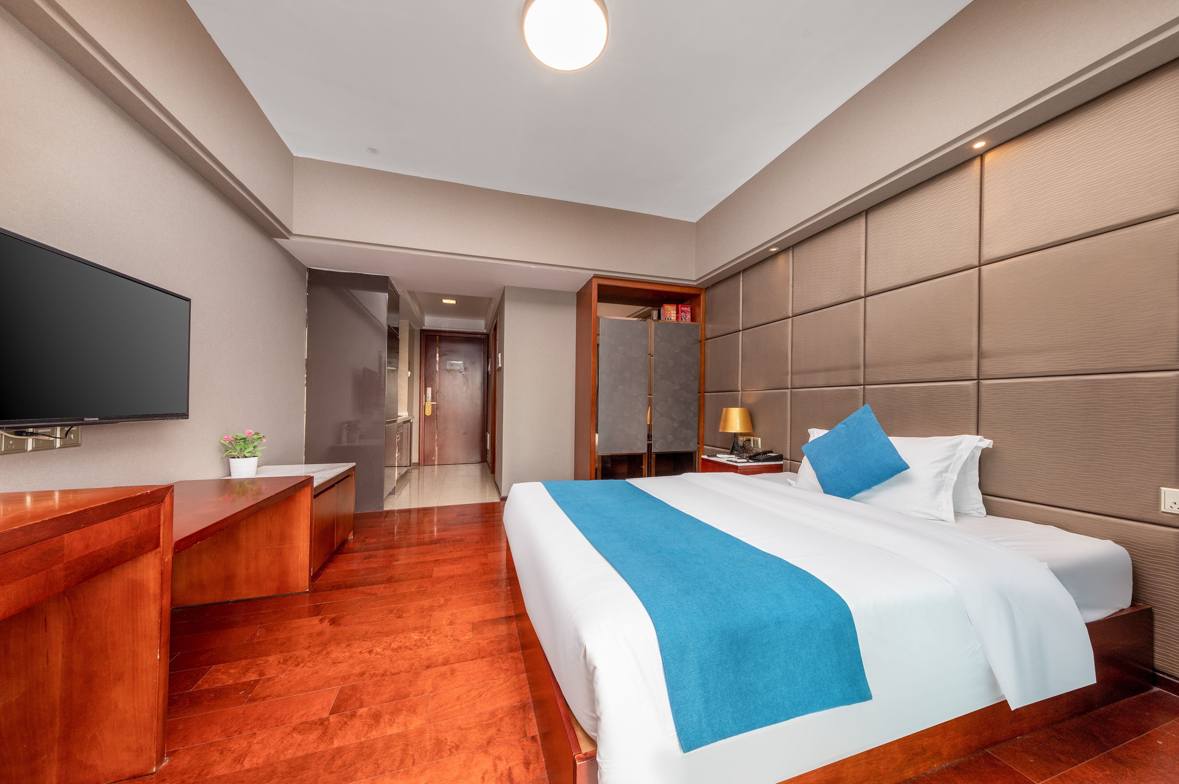 A hotel room with a large bed, a TV, a desk, and a mirror.