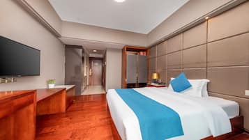 A hotel room with a large bed, a TV, a desk, and a mirror.