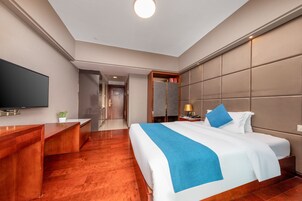 A hotel room with a large bed, a TV, a desk, and a mirror.