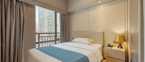 A hotel room with a bed, a nightstand, a lamp, and a view of tall buildings through the window.