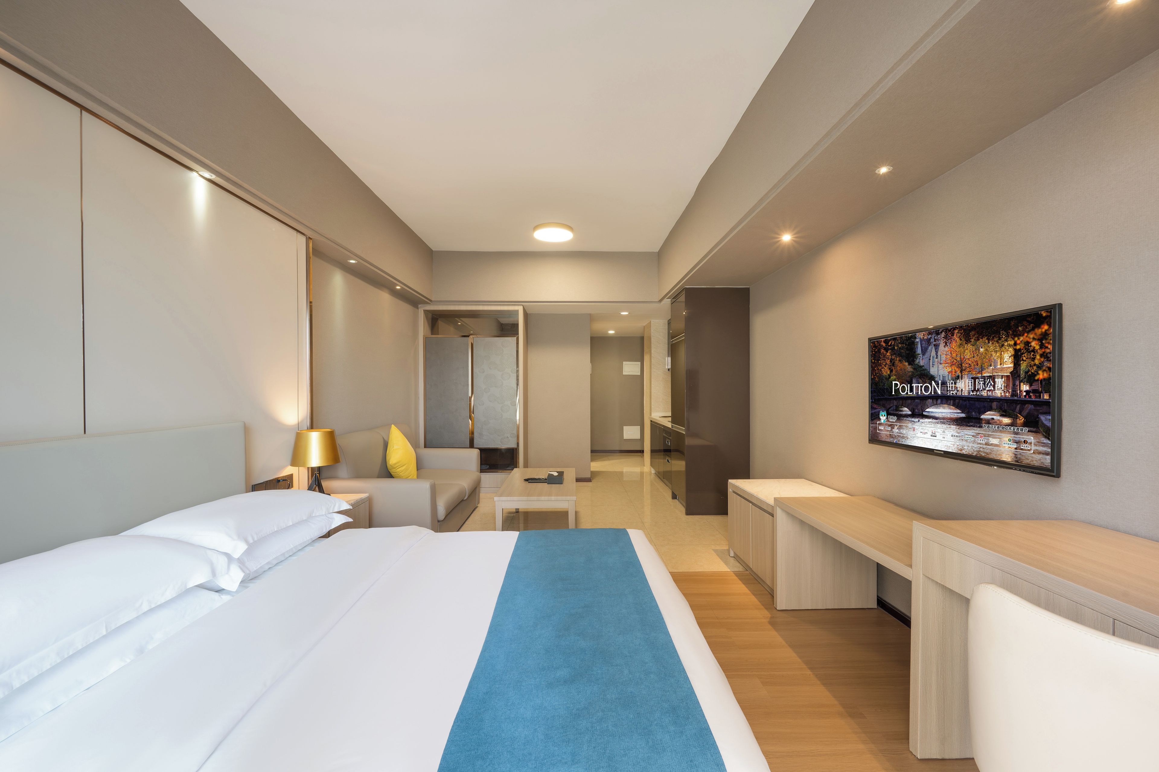 A hotel room with a bed, a desk, a television, and a bathroom visible through an open door.