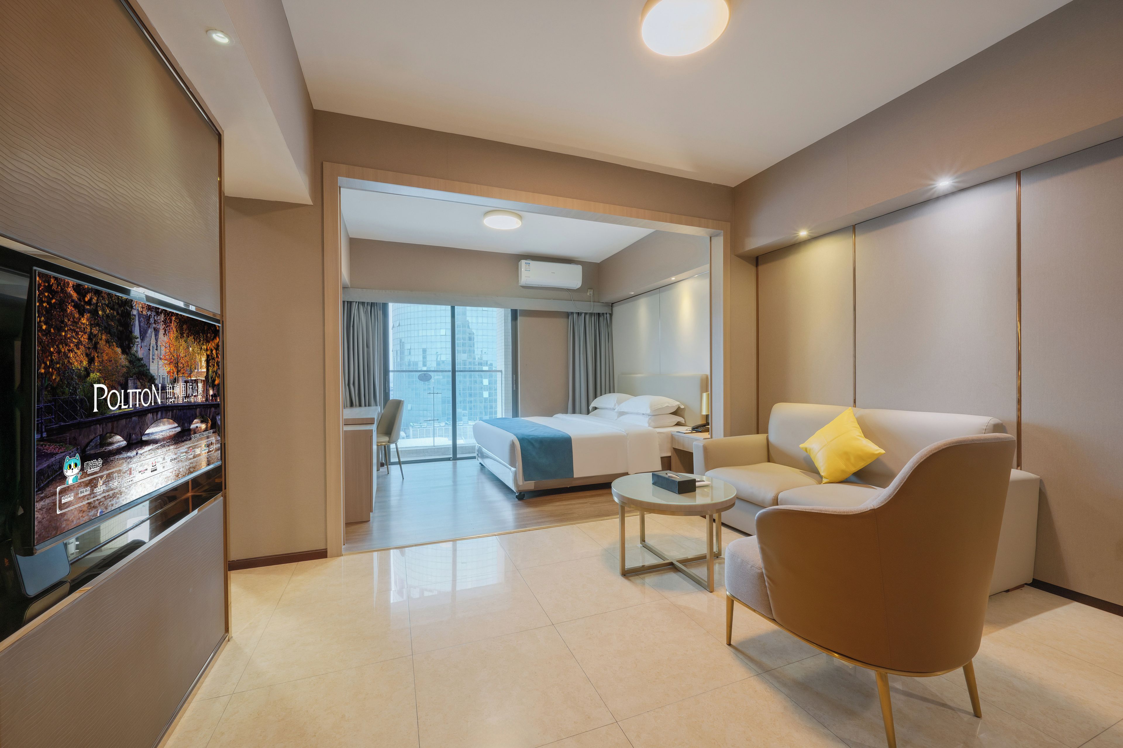 A modern hotel room with a bed, a sofa, a coffee table, and a TV.