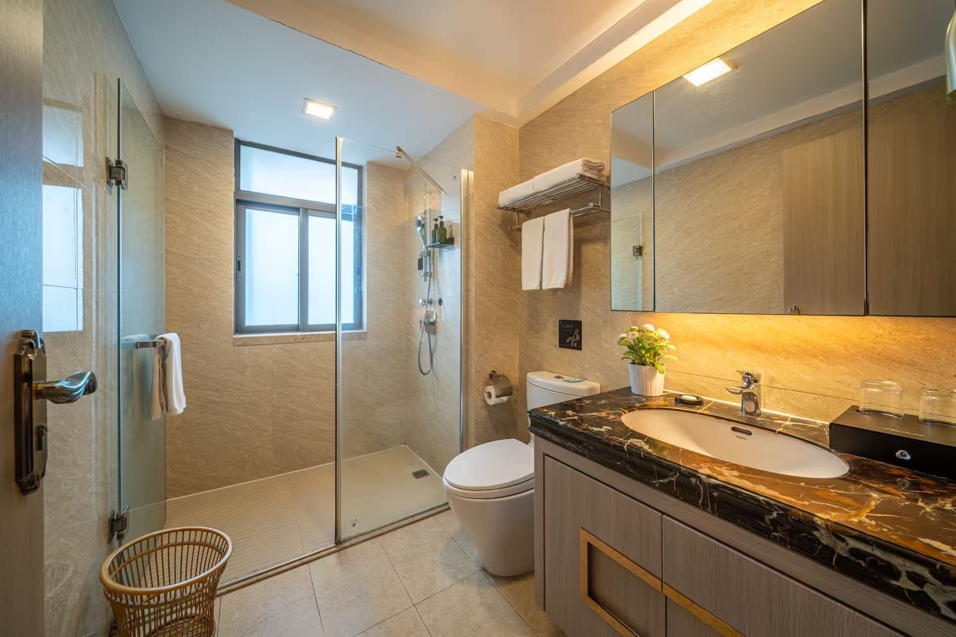 Een moderne badkamer met een douchecabine van glas, een toilet, een wastafel met een marmeren aanrechtblad en een grote spiegel.