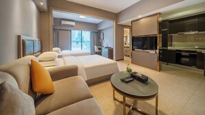 Una habitación de hotel moderna con sofá, una pequeña mesa redonda, una cama con ropa blanca, un escritorio y una kitchenette.