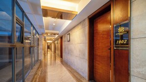 Pasillo moderno de hotel con puertas de vidrio, suelo de mármol y una puerta de madera con el número 1902.