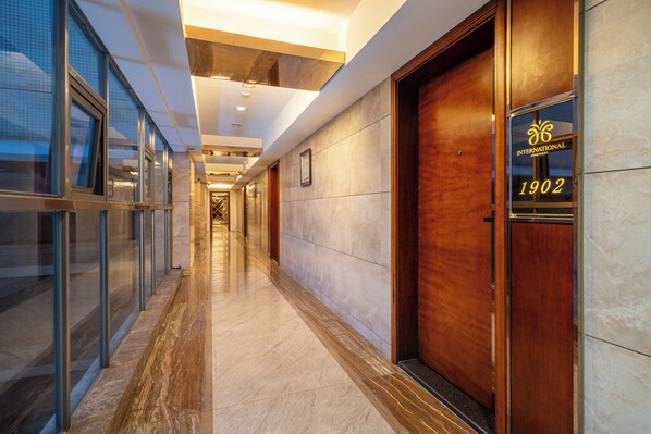 A modern hotel corridor with glass doors, a marble floor, and a wooden door with the number 1902. - Poltton International Apartment (Foshan Zumiao Lingnan Tiandi Branch) (Foshan)