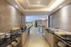 A hotel breakfast area with buffet counters, serving trays, and a long corridor leading to a room.