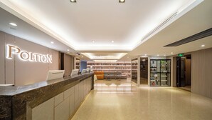 Zona de recepción de un hotel con mostrador de mármol, área de descanso con sofás y una estantería llena de libros.