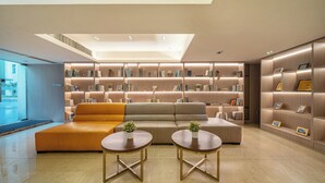 Una sala de estar moderna con un sofá, dos mesas redondas y una estantería llena de libros y cuadros enmarcados.
