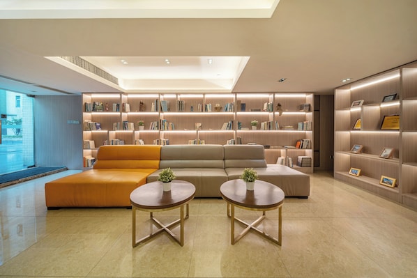 A modern living room with a sofa, two round tables, and a bookshelf filled with books and framed pictures. - Poltton International Apartment (Foshan Zumiao Lingnan Tiandi Branch) (Foshan)