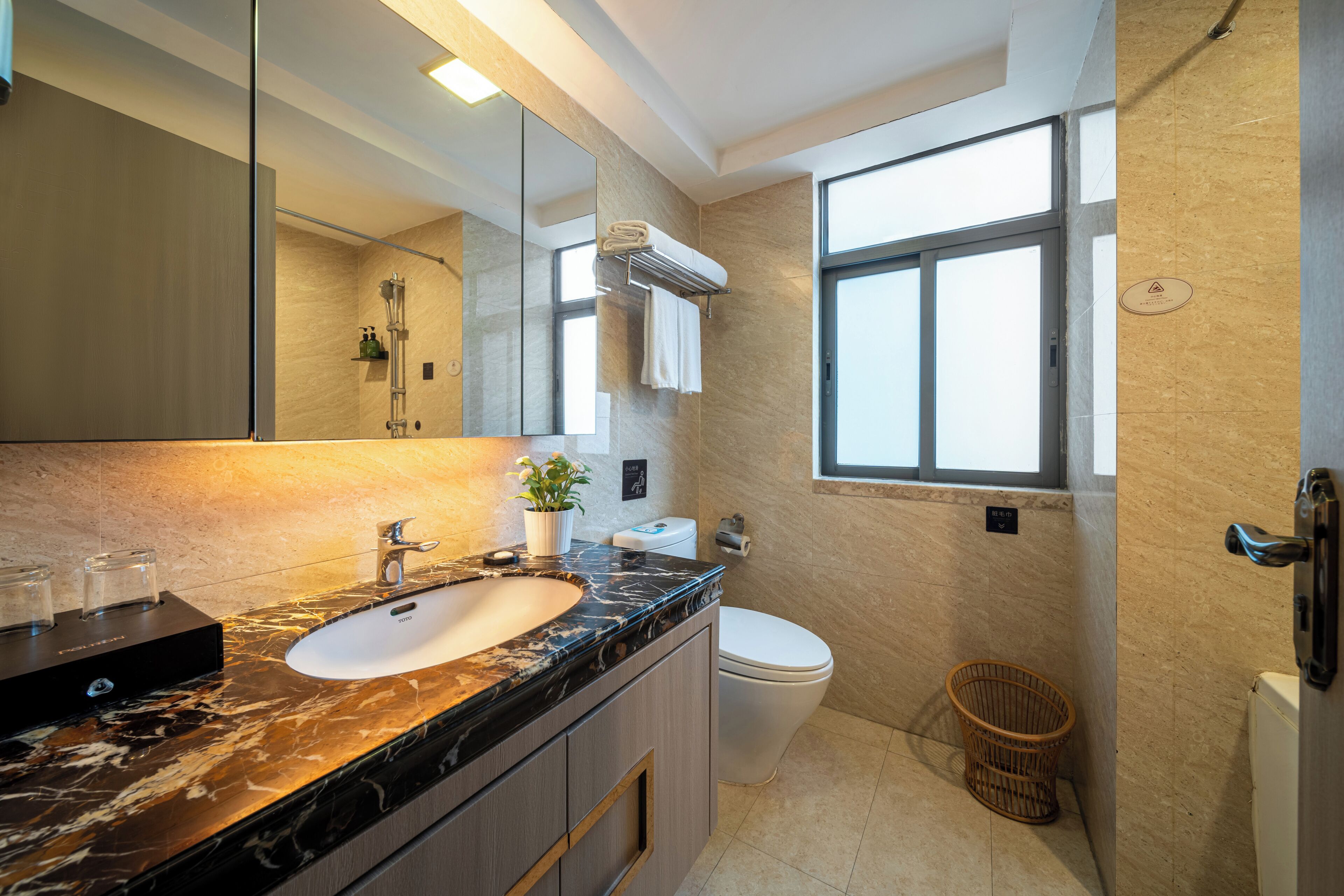 A modern bathroom with a marble sink, a large mirror, a toilet, and a window providing natural light.