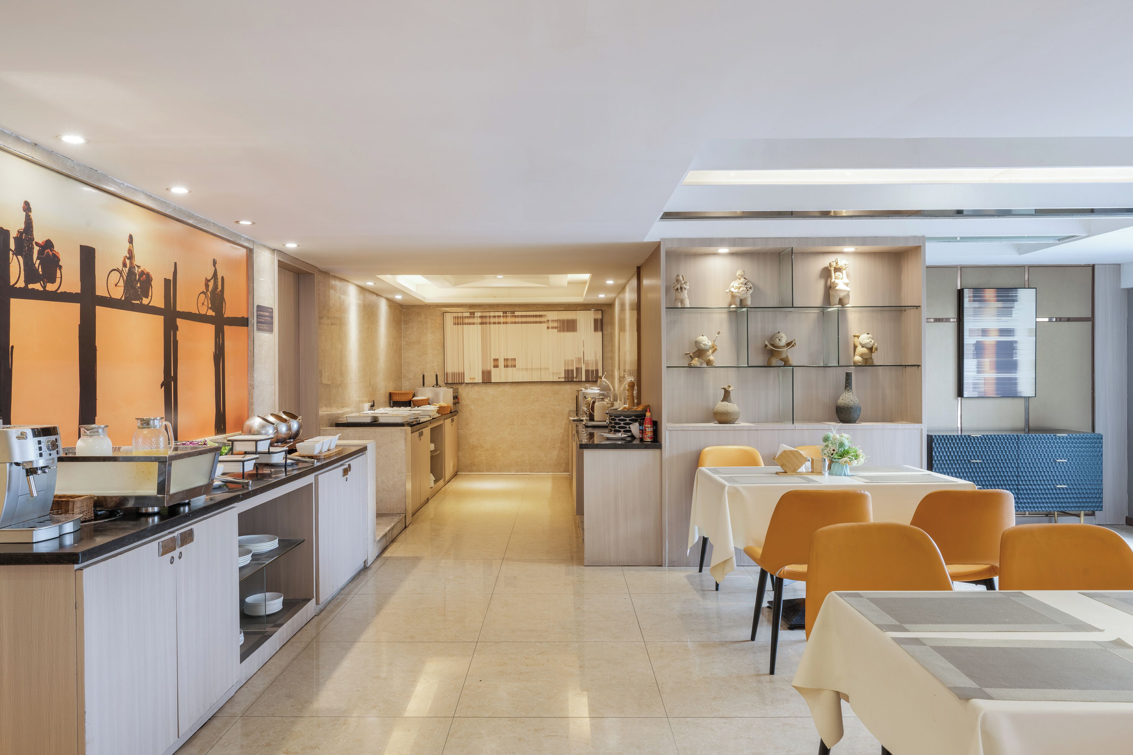 Een moderne hotel eetruimte met een buffetopstelling, een zithoek met tafels en stoelen, en een decoratieve wand met beeldjes.
