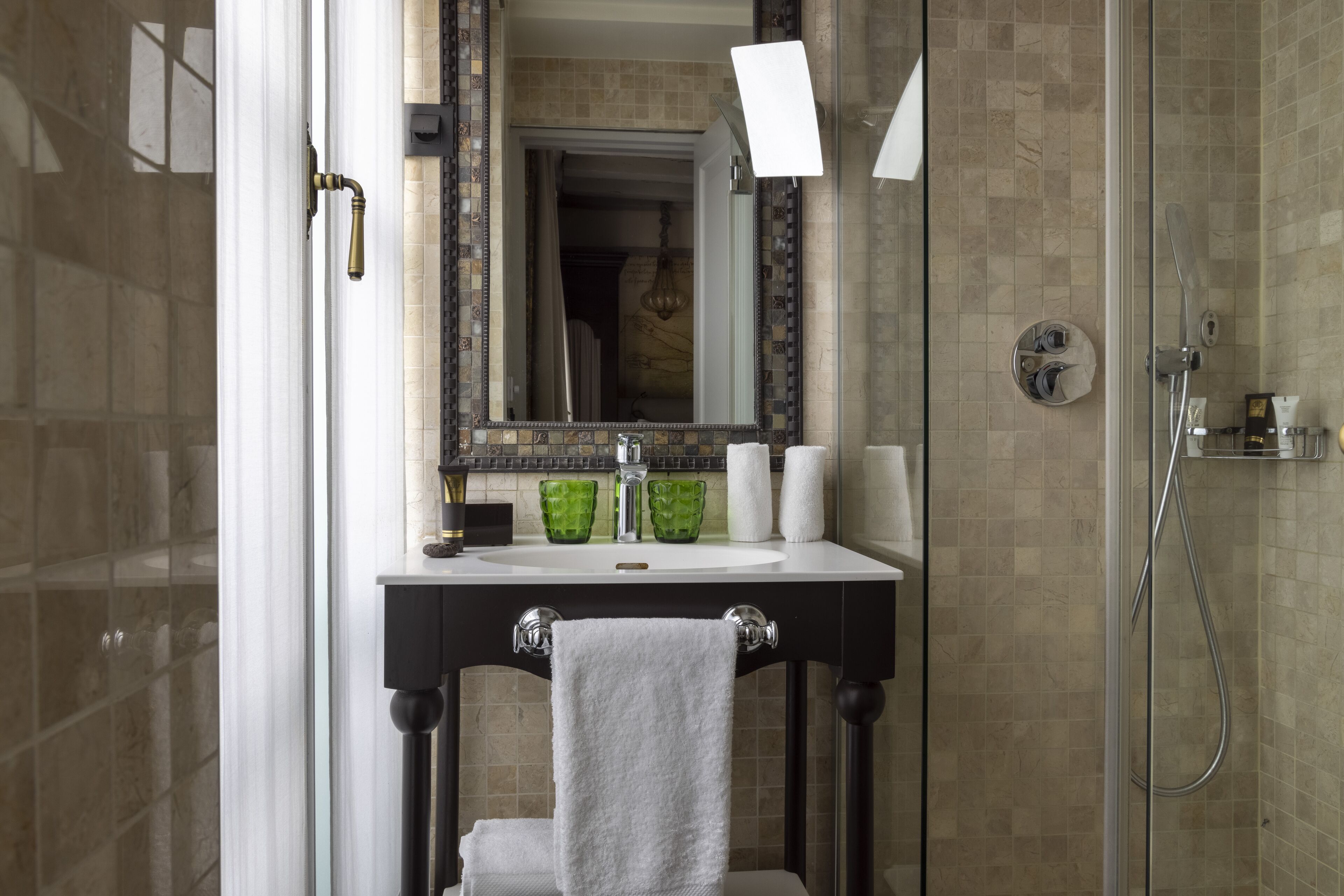 A bathroom with a glass shower enclosure, a white sink with a black countertop, and a mirror with a decorative frame.