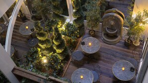 Un jardín interior con plantas en macetas y mesas redondas con velas.