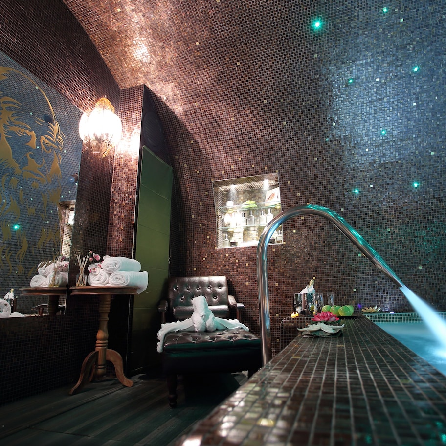 A spa room with a massage chair, a small table with towels and candles, and a wall with a mosaic design.