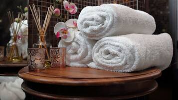 A wooden table with rolled white towels, decorative glass bottles with reed diffusers, and pink orchids.