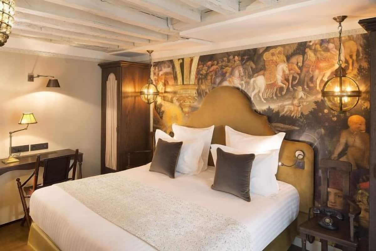 A hotel room with a large bed, a desk, a lamp, and a mural on the wall.
