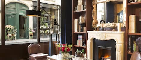 A cozy room with a fireplace, bookshelves, a leather armchair, and a view of the street outside.