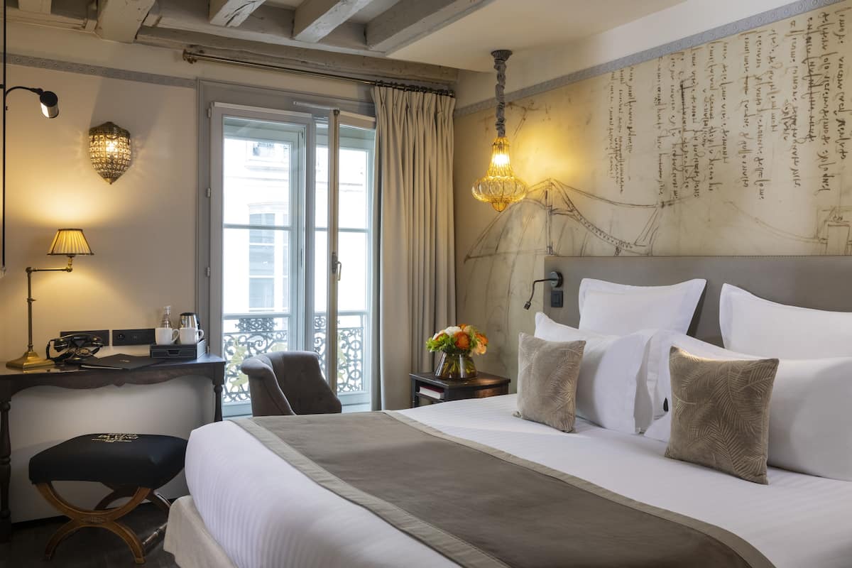 A hotel room with a large bed, a desk with a lamp, a chair, and a view of the outside.