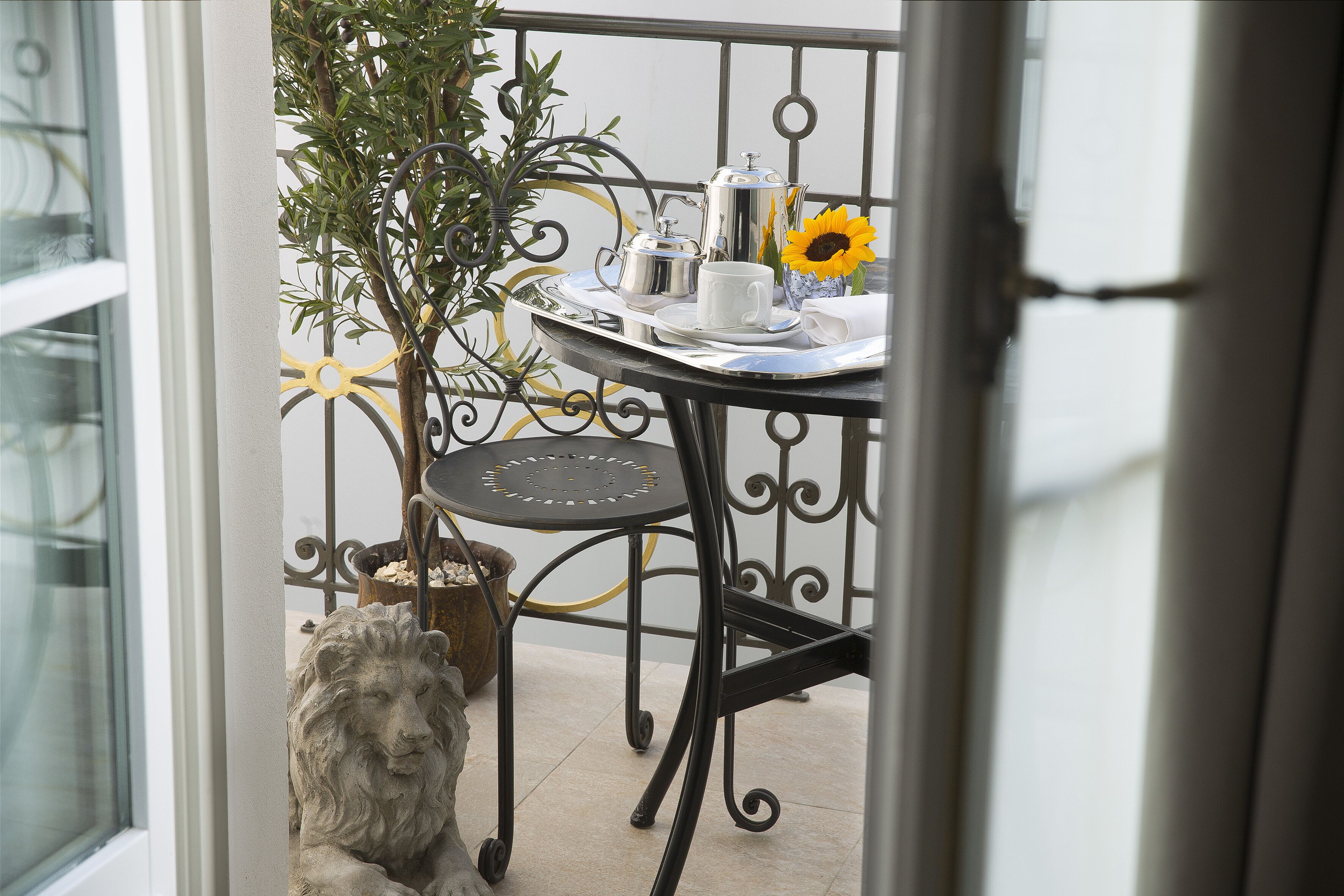 Een balkon met een metalen tafel gedekt voor thee, een bloempot en een beeld van een leeuw.