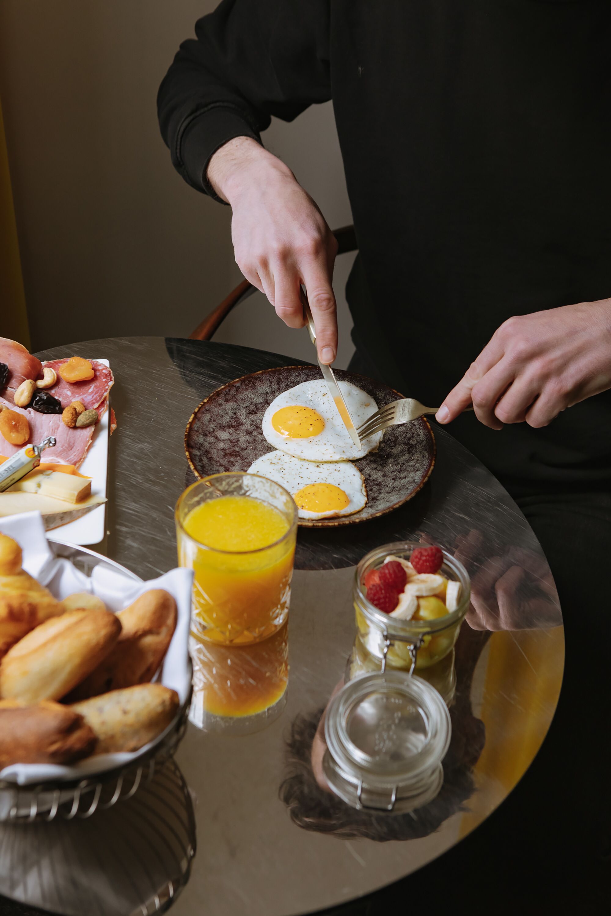 Un desayuno con huevos, pasteles y un vaso de jugo de naranja sobre una mesa.