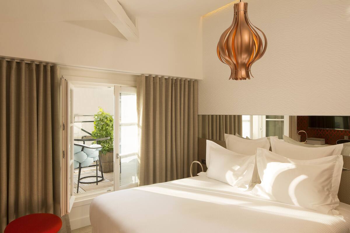 Une chambre d’hôtel avec un lit, des rideaux, une télévision et un balcon équipé d’une chaise et d’une plante.