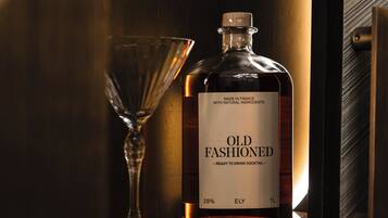 A bottle of Old Fashioned whiskey and a glass on a shelf.