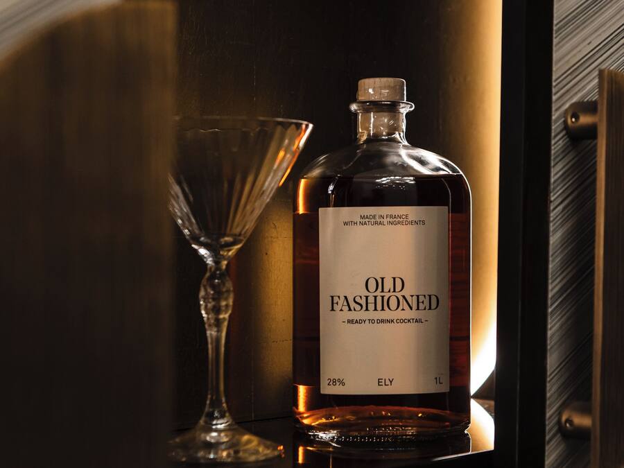 A bottle of Old Fashioned whiskey and a glass on a shelf.
