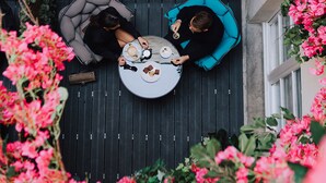 A balcony with two people seated on chairs, surrounded by lush pink flowers. - Hôtel Dupond Smith (Paris)