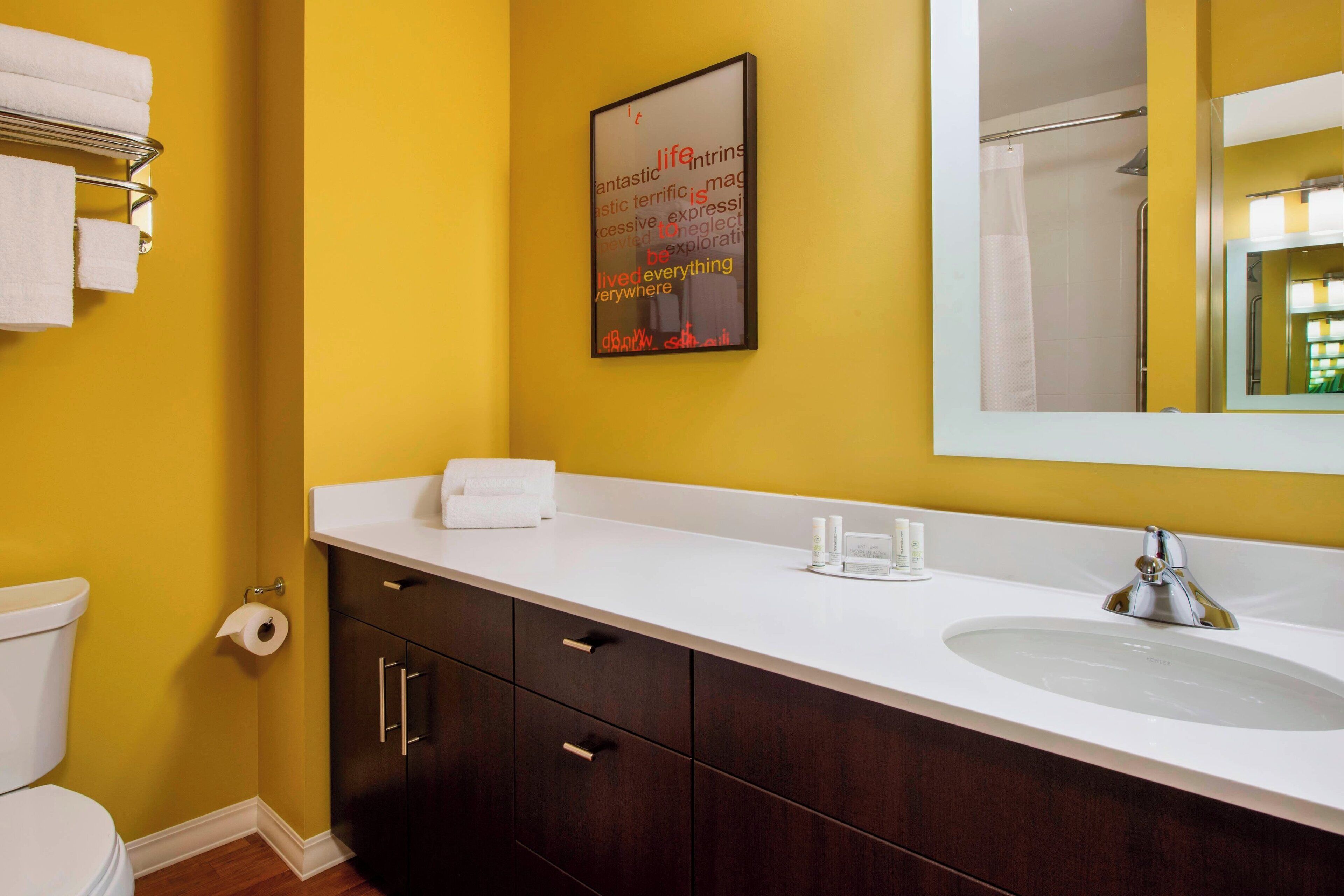Un baño con pared amarilla, lavamanos blanco y armarios de madera oscura.